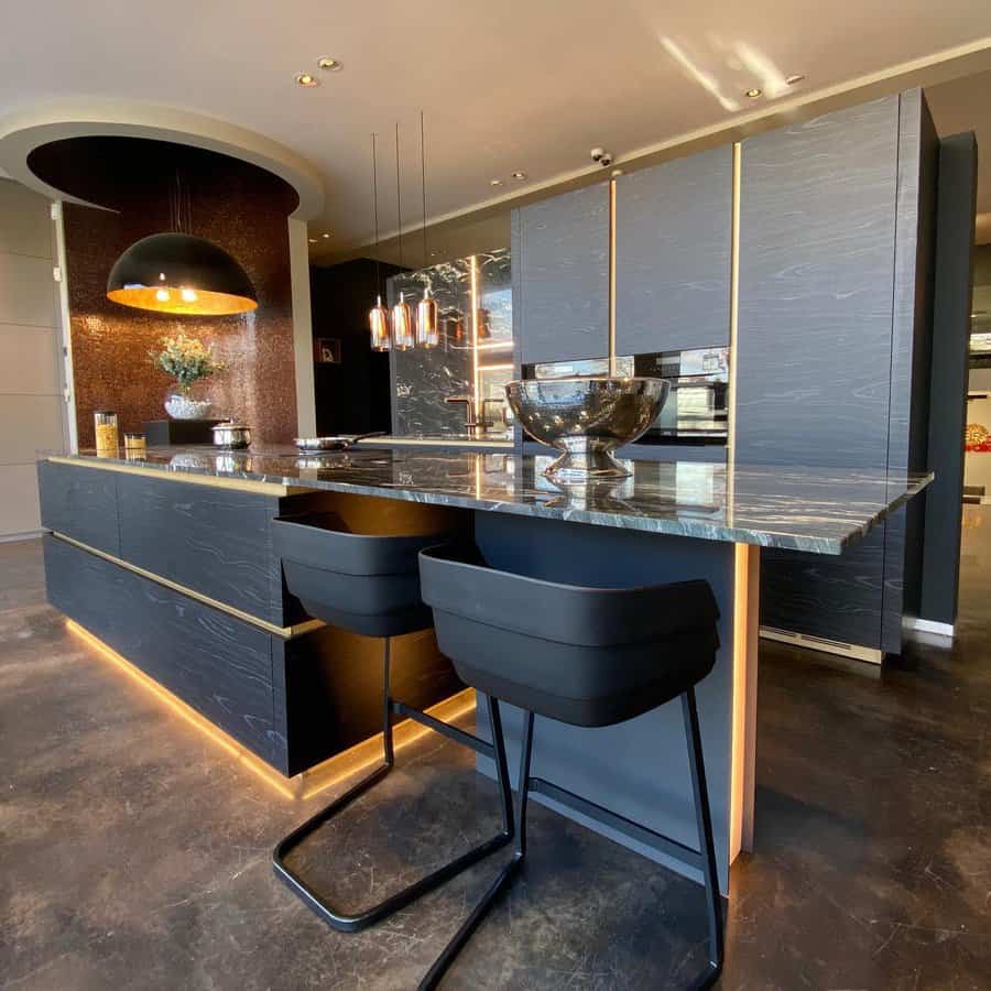 Modern kitchen with dark cabinetry, marble island, black bar stools, and LED strip lighting