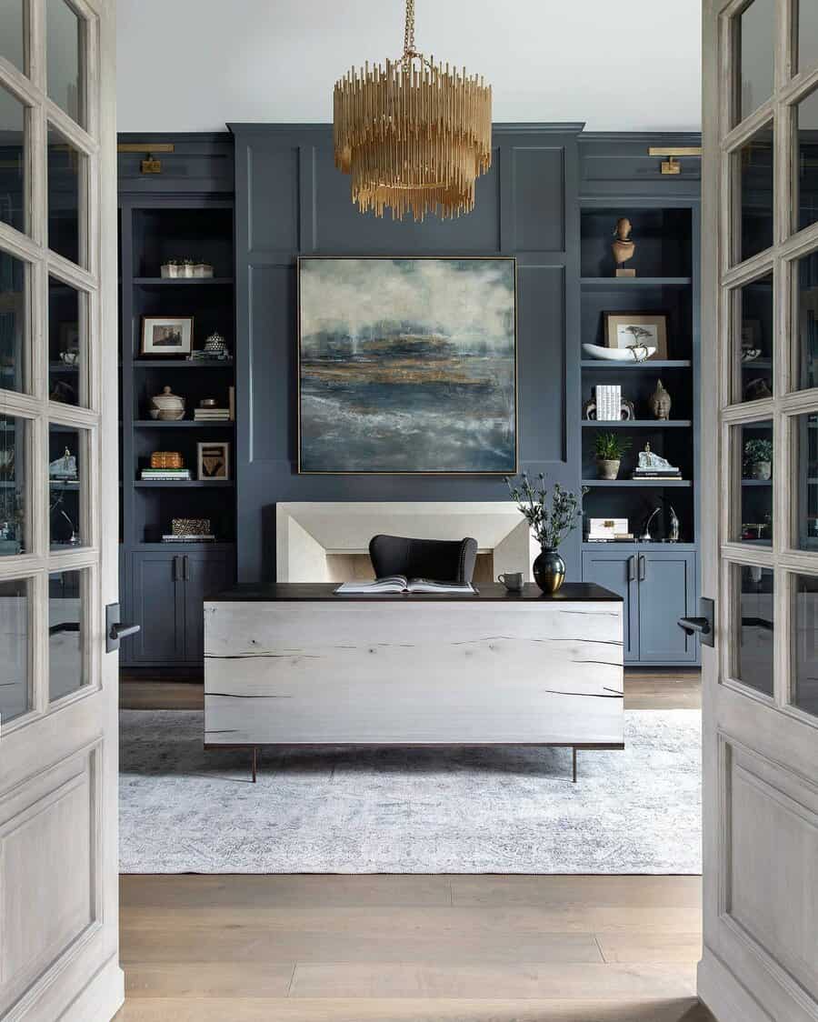 Home office with modern decor, abstract painting, and navy built-in shelves featuring a large chandelier above the central desk