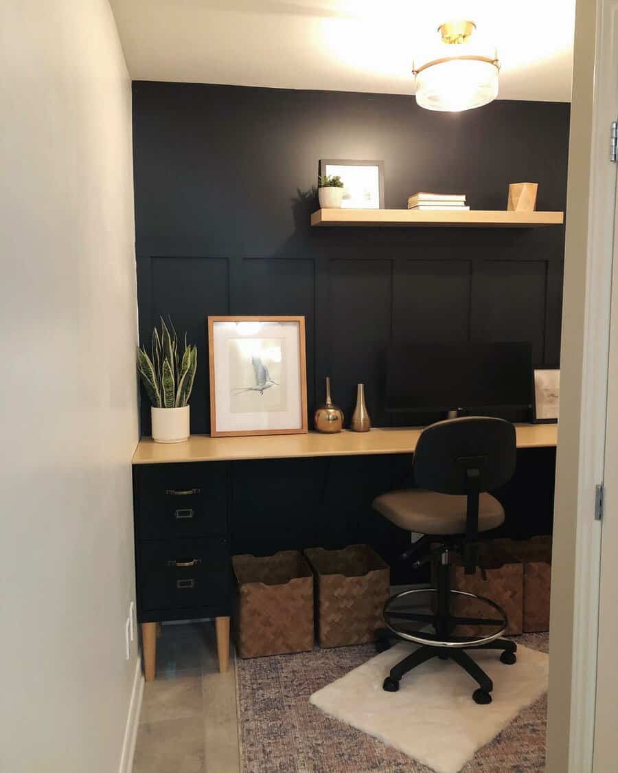 Small home office with a wooden desk, chair, computer, plant, framed picture, shelf, and baskets on a light-patterned rug