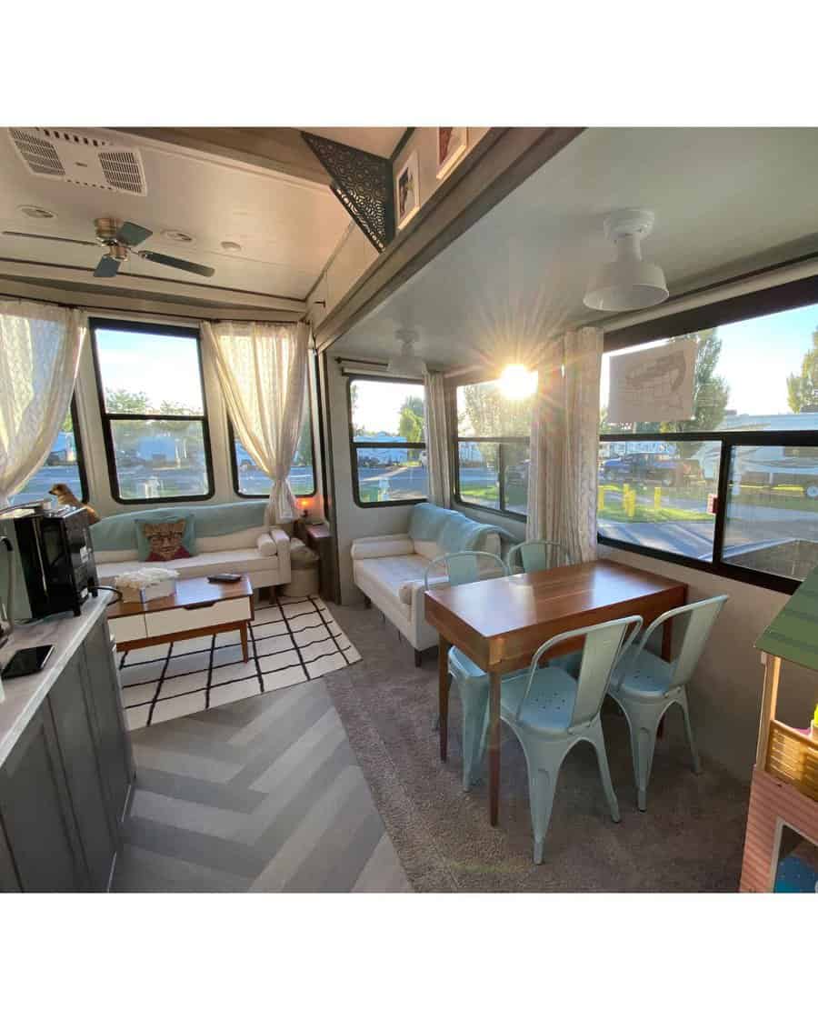 A bright and airy RV living area with soft seating, a wooden dining table with metal chairs, and natural sunlight streaming through the windows, creating a relaxed and welcoming space.