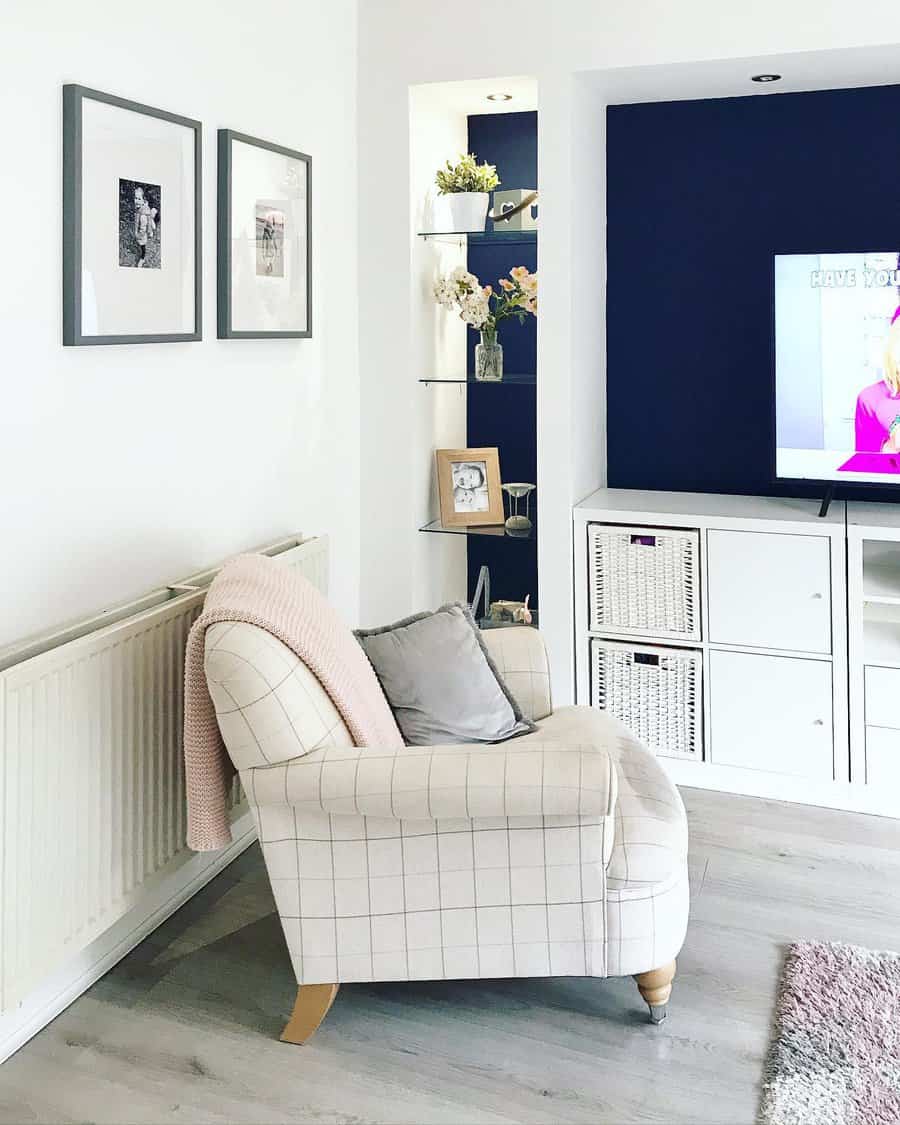 A cozy living room with a plaid armchair, built-in shelving, wicker basket storage, and a navy accent wall for a stylish and functional space