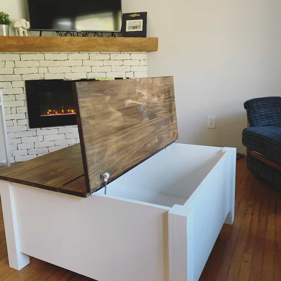 White storage box with an open wooden lid in a living room, near a brick fireplace with a TV on the mantel