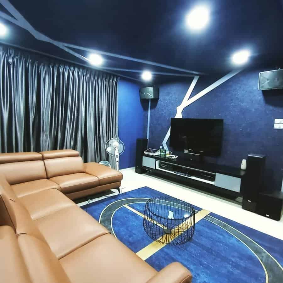 Modern living room with brown leather sofas, blue walls, a large TV on a stand, ceiling lights, and a blue area rug with a geometric design