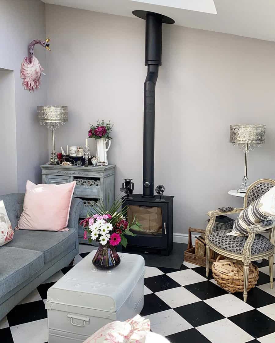 Elegant living room with a black wood stove, checkered flooring, vintage decor, and soft pastel accents for a cozy yet stylish ambiance.