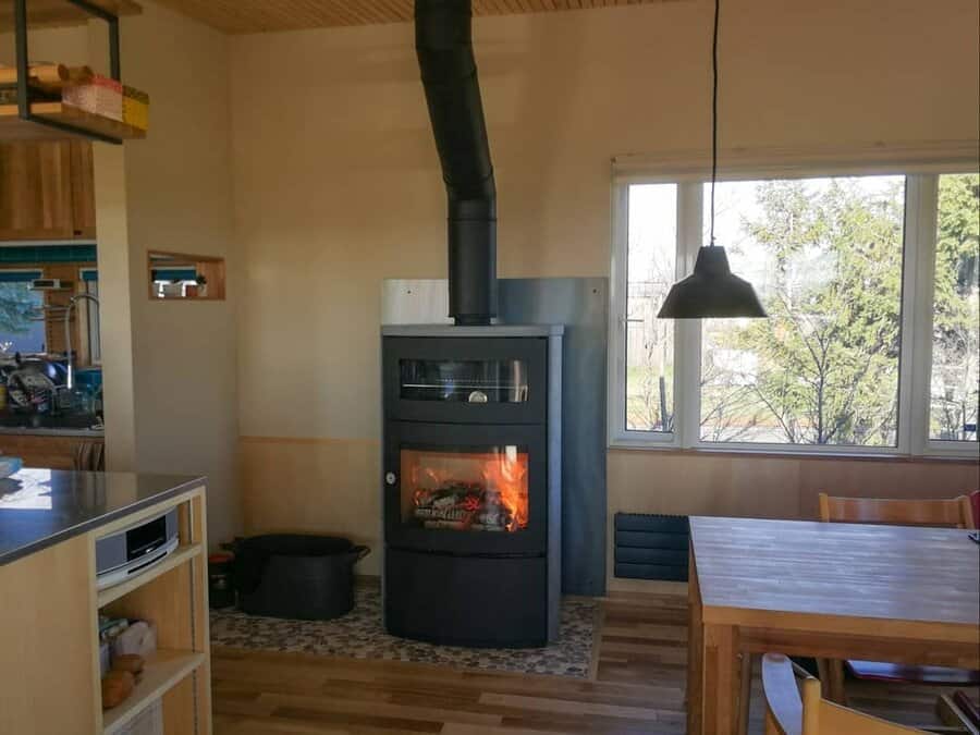 Modern wood stove with a built-in oven, set in a cozy open-concept dining area with warm wood accents and large windows for natural light.