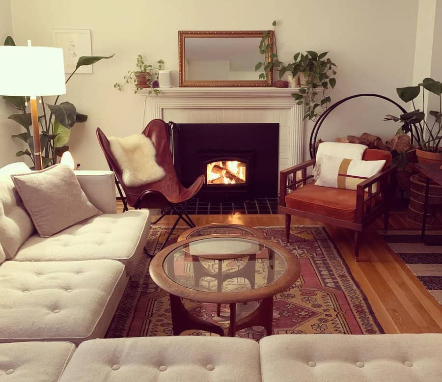 Cozy living room with a wood stove insert in a white mantel fireplace, warm-toned furniture, layered rugs, and lush greenery for a relaxed vibe.