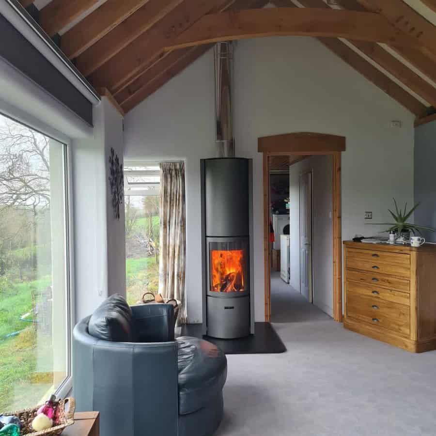 Modern wood stove with a sleek cylindrical design, set against a vaulted ceiling with exposed beams, creating a warm and inviting atmosphere.