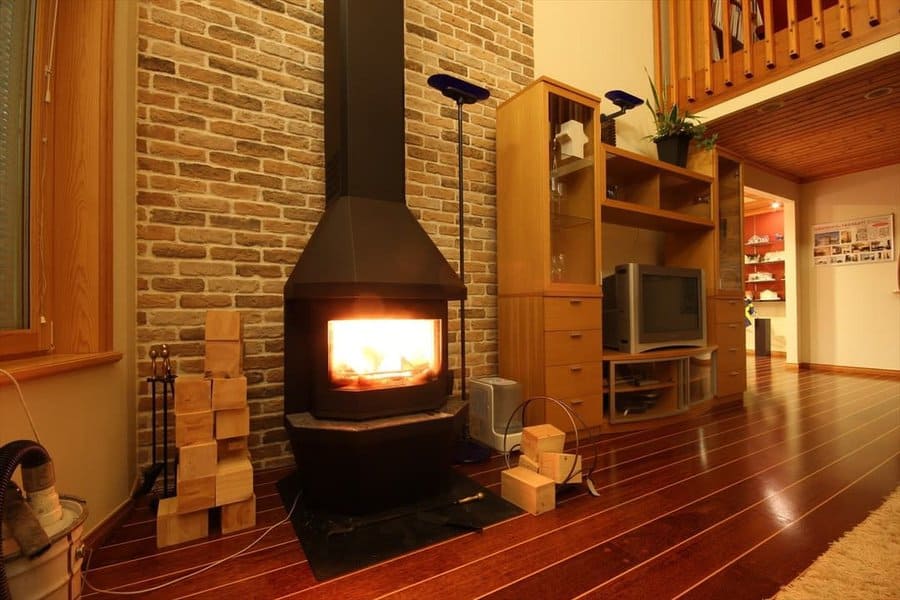 Cozy living room with a vintage wood stove, exposed brick wall, and warm wood flooring, creating a rustic and inviting atmosphere.