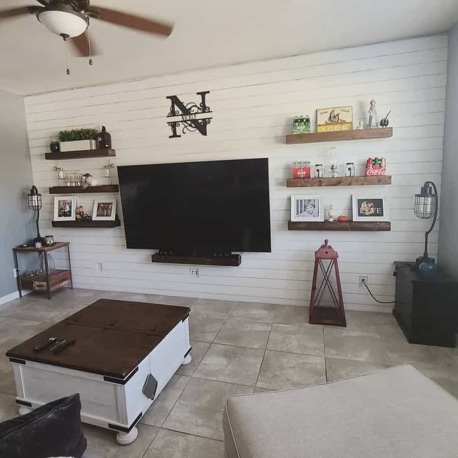 Living room with a wall-mounted TV, shelving with decor, a coffee table, and ceiling fan; neutral colors and a tiled floor