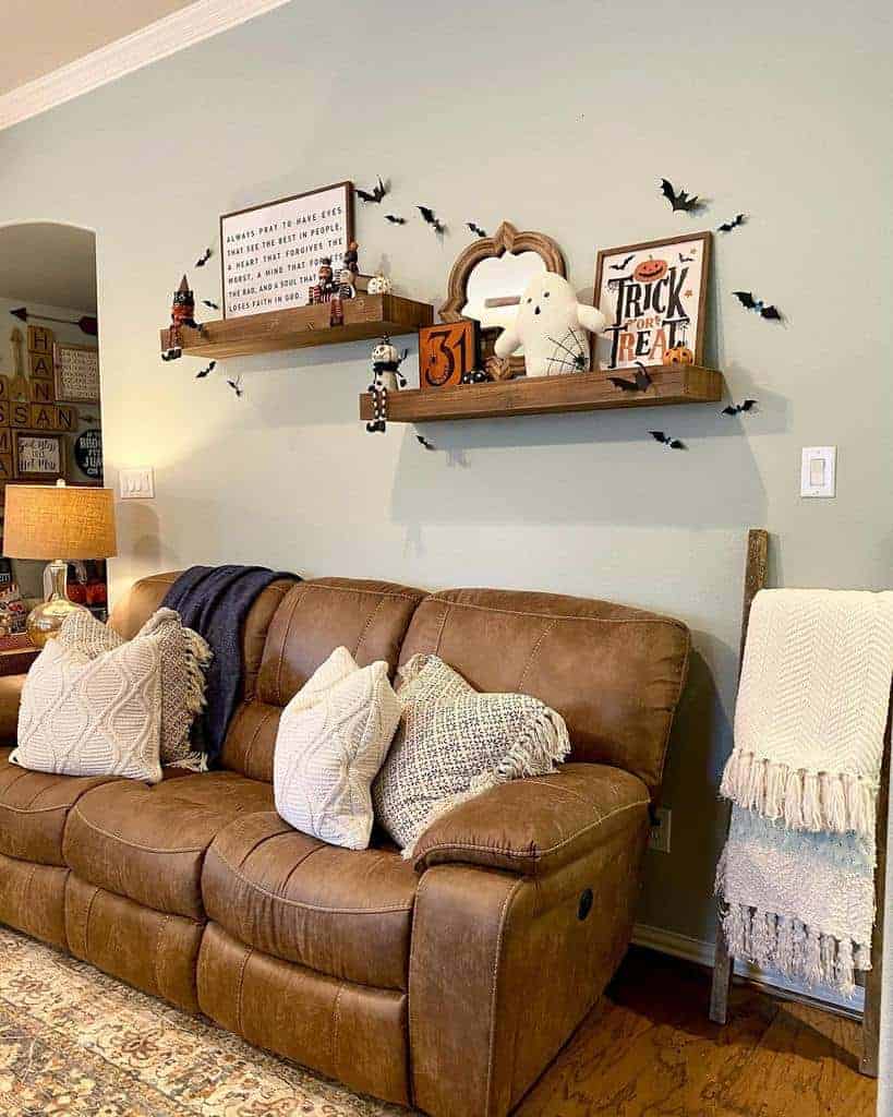 Cozy living room with Halloween-themed shelves above a brown leather sofa, featuring bats, a ghost, and fall decorations