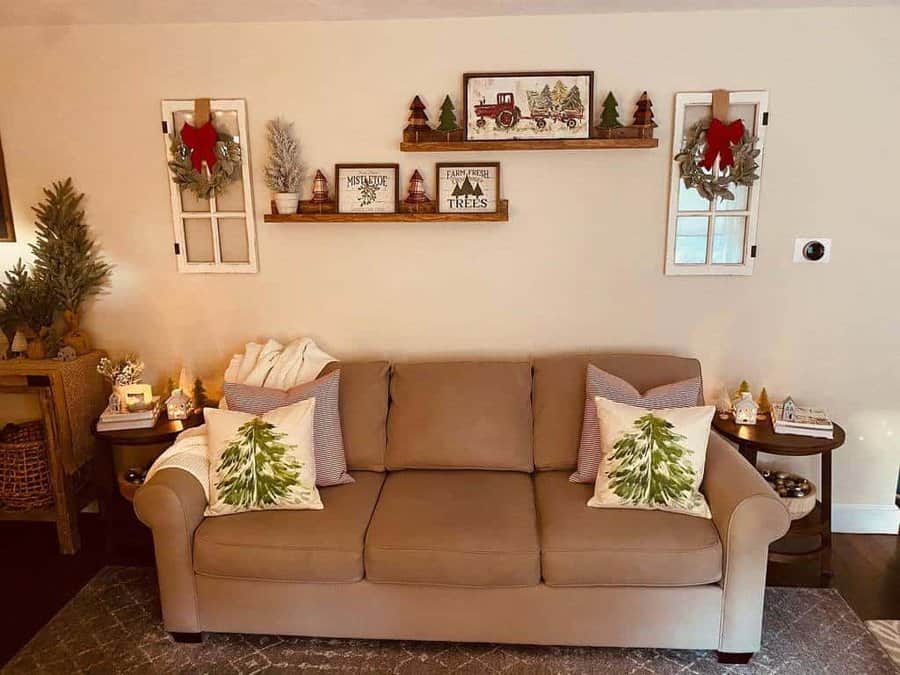 Festive living room with a beige sofa, Christmas pillows, and decorated shelves above featuring holiday decor such as wreaths and mini trees