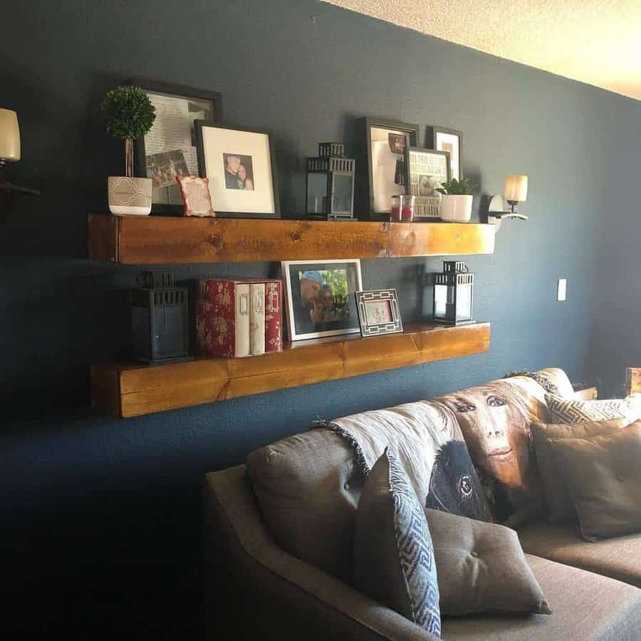 Living room with navy walls, floating wooden shelves displaying framed photos, small plants, and lanterns, a gray couch with cushions