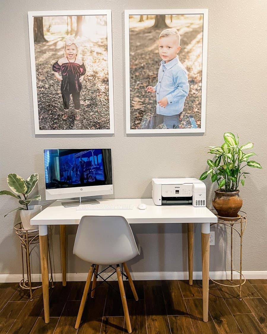 Home workspace with a white desk, computer, and printer; two framed photos of children on the wall and two potted plants on each side