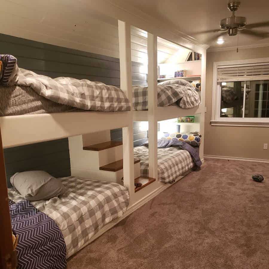 Cozy room with two sets of bunk beds, gray plaid bedding, built-in stairs, carpeted floor, and a window with blinds