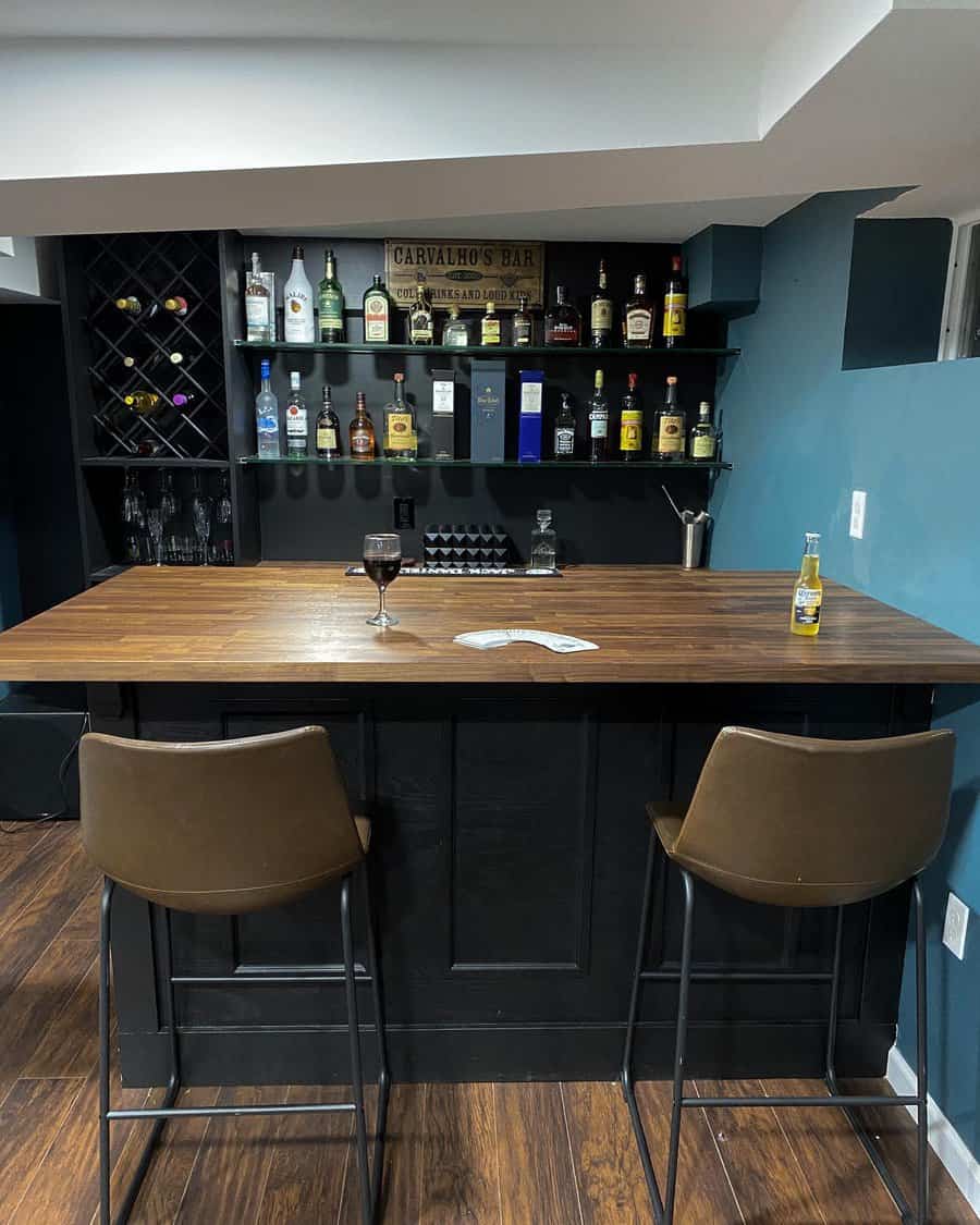 Cozy basement bar with dark cabinetry, wooden countertops, built-in shelving, and warm lighting for an intimate and stylish entertainment space.