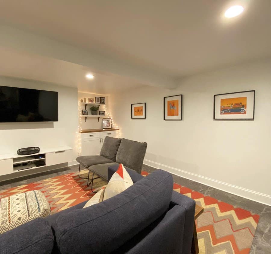 Cozy basement lounge with a low ceiling, warm lighting, built-in shelving, and colorful decor for a stylish and inviting entertainment space.