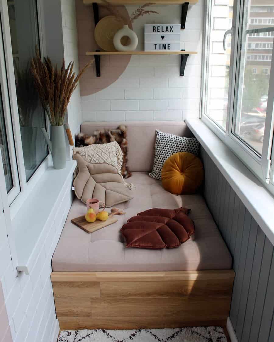 Cozy enclosed balcony with a built-in cushioned bench, decorative pillows, and a small wooden tray holding a cup and fruit. A 'Relax Time' sign sits on floating shelves, adding a warm and inviting touch.