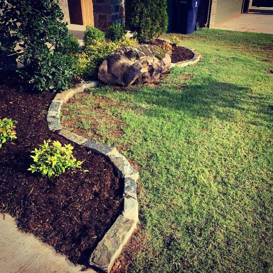 Low-maintenance front yard with a neatly edged mulch bed, vibrant plants, a large decorative rock, and a well-manicured lawn