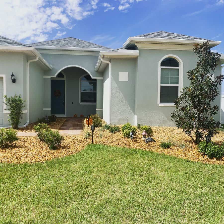 Charming front yard with a neatly manicured lawn, rock mulch landscaping, scattered shrubs, and a welcoming arched entryway