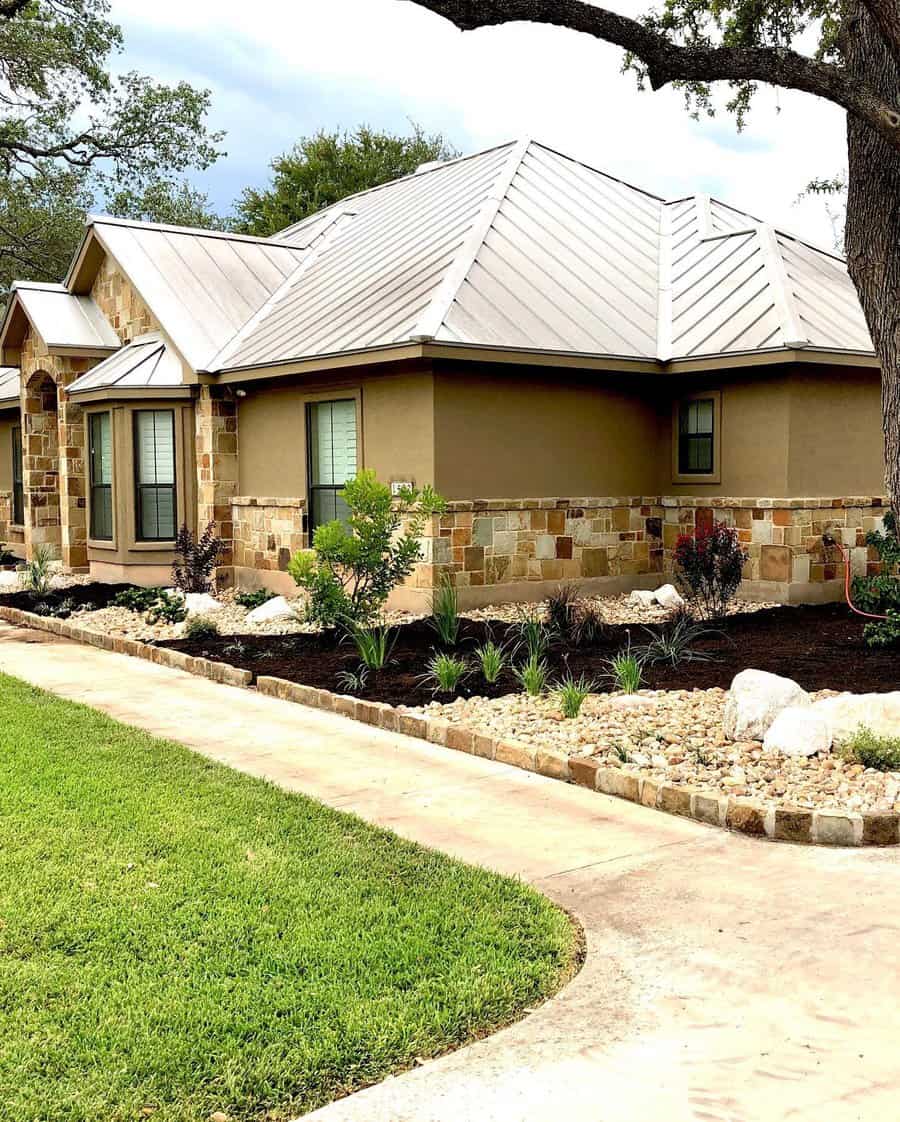 Modern front yard with a clean mulch bed, drought-tolerant plants, stone accents, and a well-maintained lawn beside a stone house