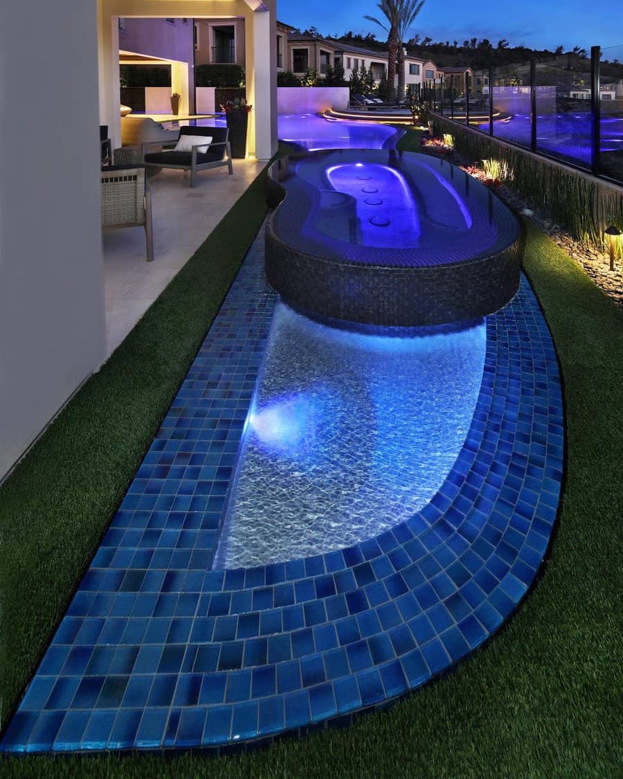 Luxurious outdoor space with a modern illuminated pool, whirlpool section, and elegant seating area surrounded by greenery