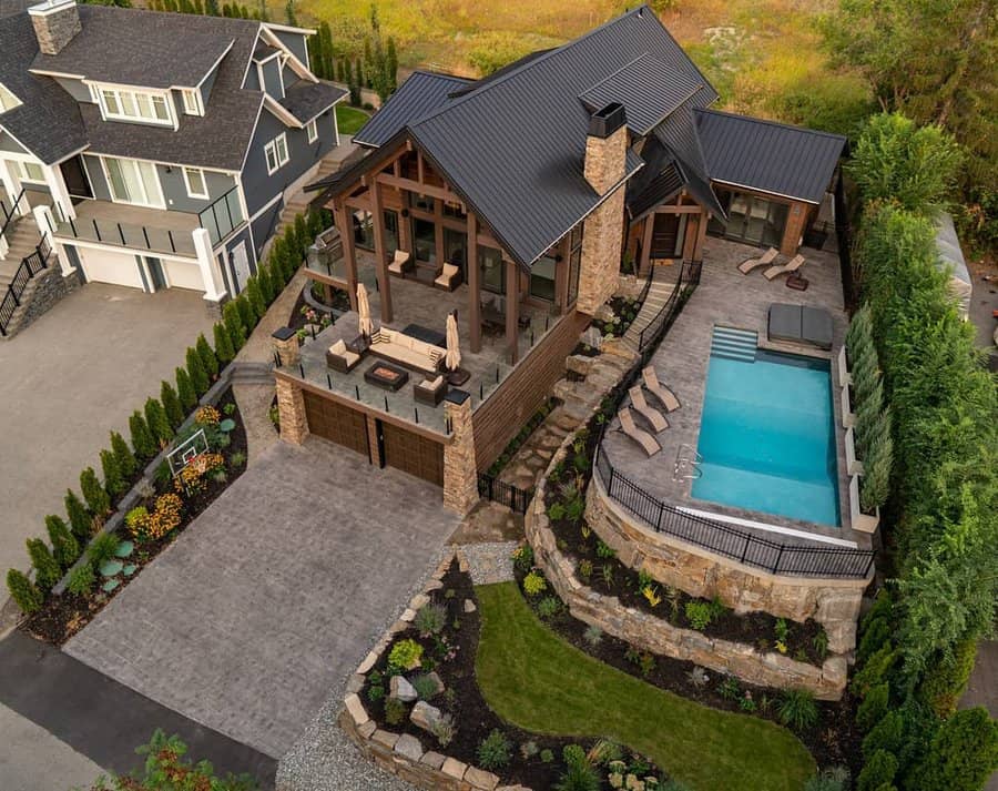 Aerial view of a modern house with a pool, spacious patio, landscaping, and a stone and wood facade