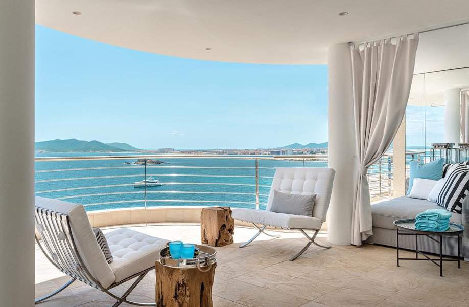 Luxurious balcony with modern chairs, a wooden table, and ocean view, curtains and a lounger with towels add to the relaxing atmosphere