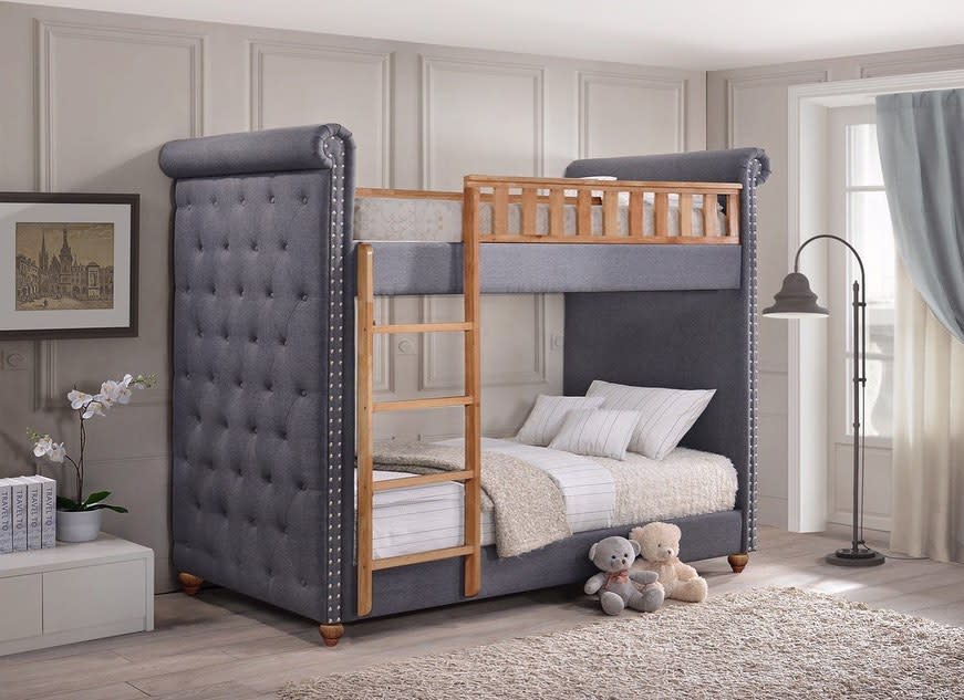 Stylish bunk bed with plush gray upholstery, wooden ladder, and cozy bedding in a bright room with a floor lamp and two stuffed bears