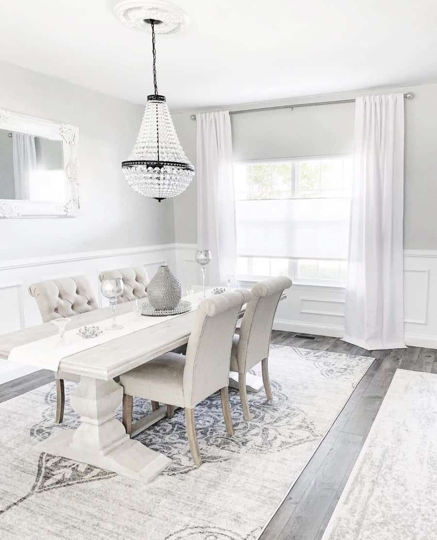 Elegant dining room with a chandelier, white table, beige tufted chairs, large mirror, and window with sheer curtains