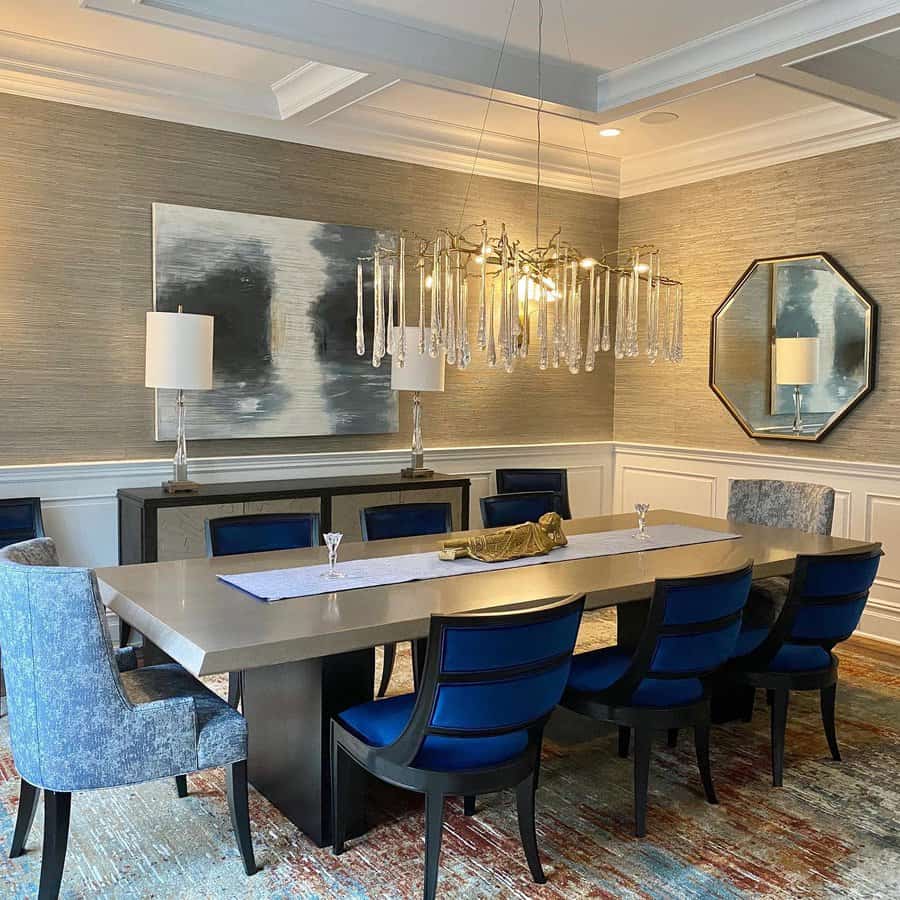 Dining room with a long table, blue chairs, modern chandelier, abstract wall art, and an octagonal mirror