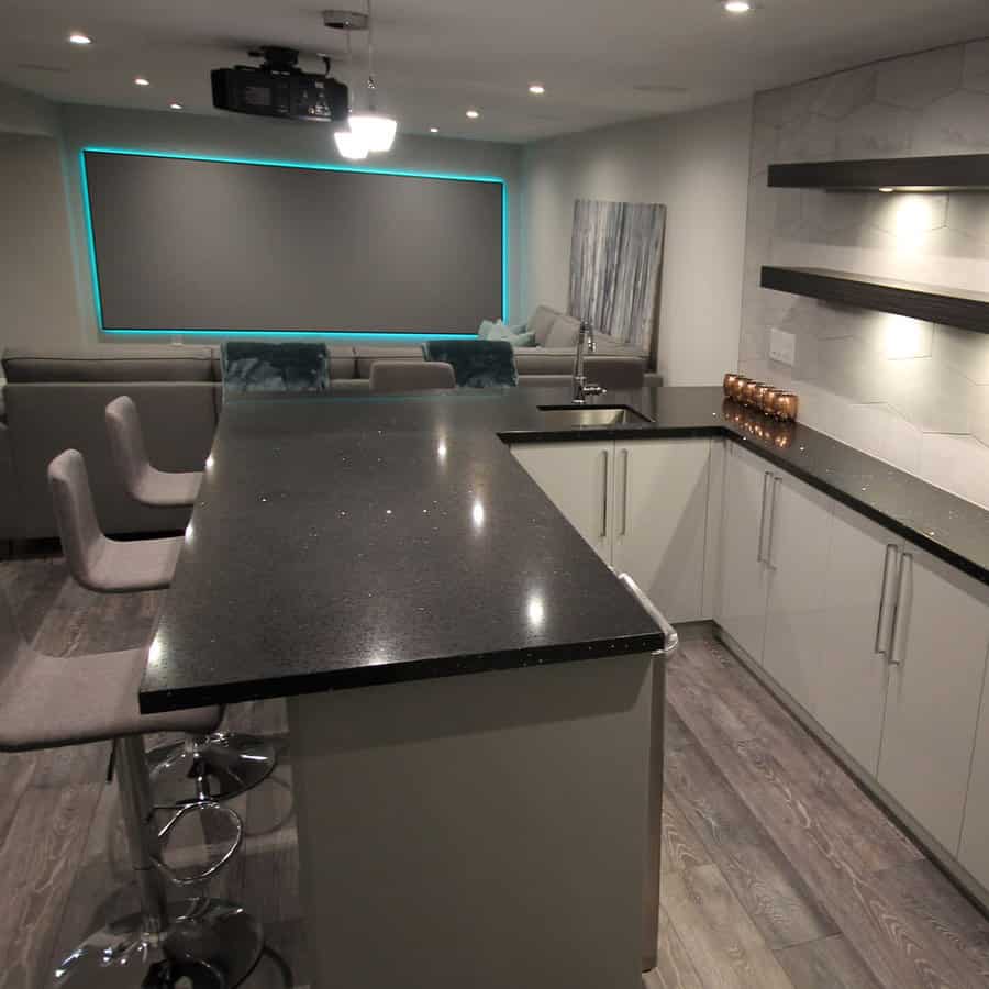 Sleek and modern basement with a home theater, illuminated screen, stylish bar area, and dark quartz countertops for a luxurious entertainment space.