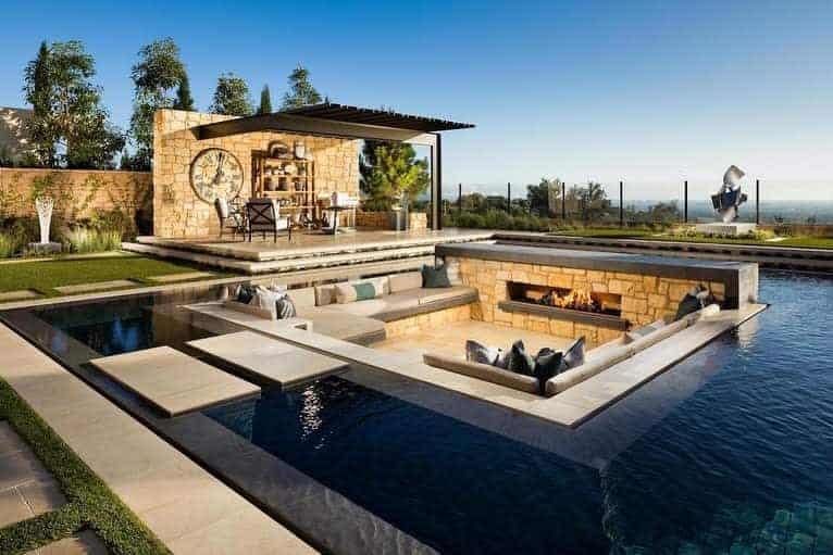 Luxury outdoor setup with a sunken fire pit lounge surrounded by a modern pool, stone accents, and a stylish pergola dining area