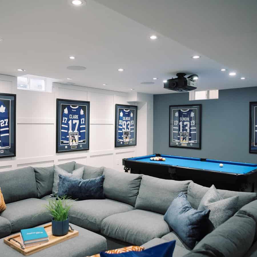 Stylish basement man cave with a large sectional, framed sports memorabilia, a pool table, and a projector for the ultimate entertainment space.