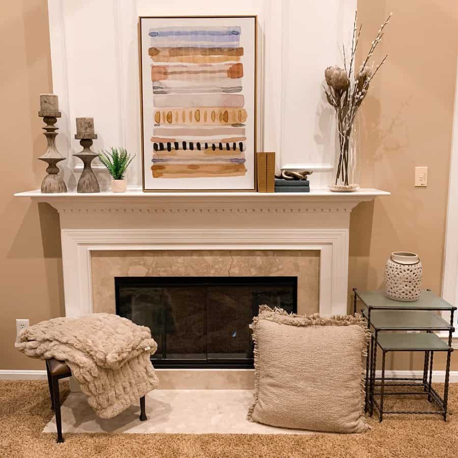 Cozy living room with a white fireplace, abstract artwork, decorative candles, a soft blanket, cushions, and a small plant