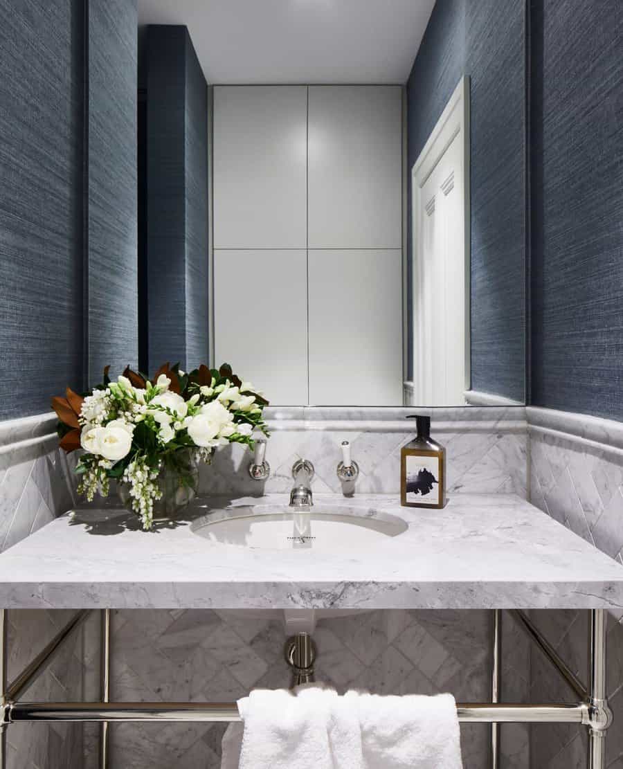 Elegant bathroom with white marble vanity and backsplash, wall-mounted faucet, navy textured walls, and fresh white floral arrangement.