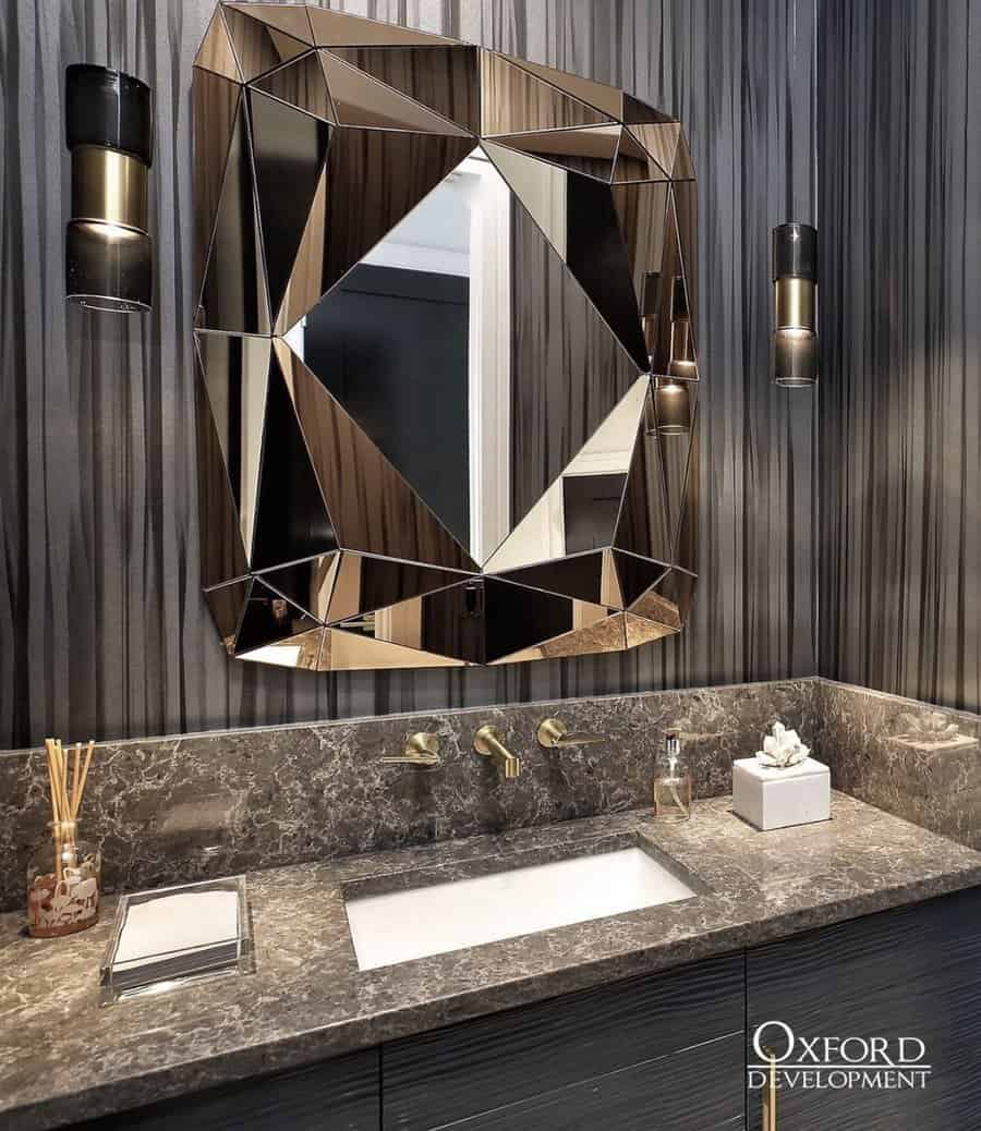 Luxurious bathroom with dark marble backsplash, faceted geometric mirror, gold fixtures, and striped textured wall panels.