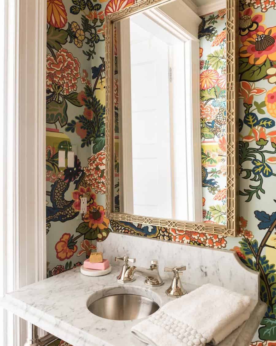 Vibrant bathroom with colorful floral wallpaper, white marble vanity and backsplash, silver fixtures, and a detailed gold-framed mirror.