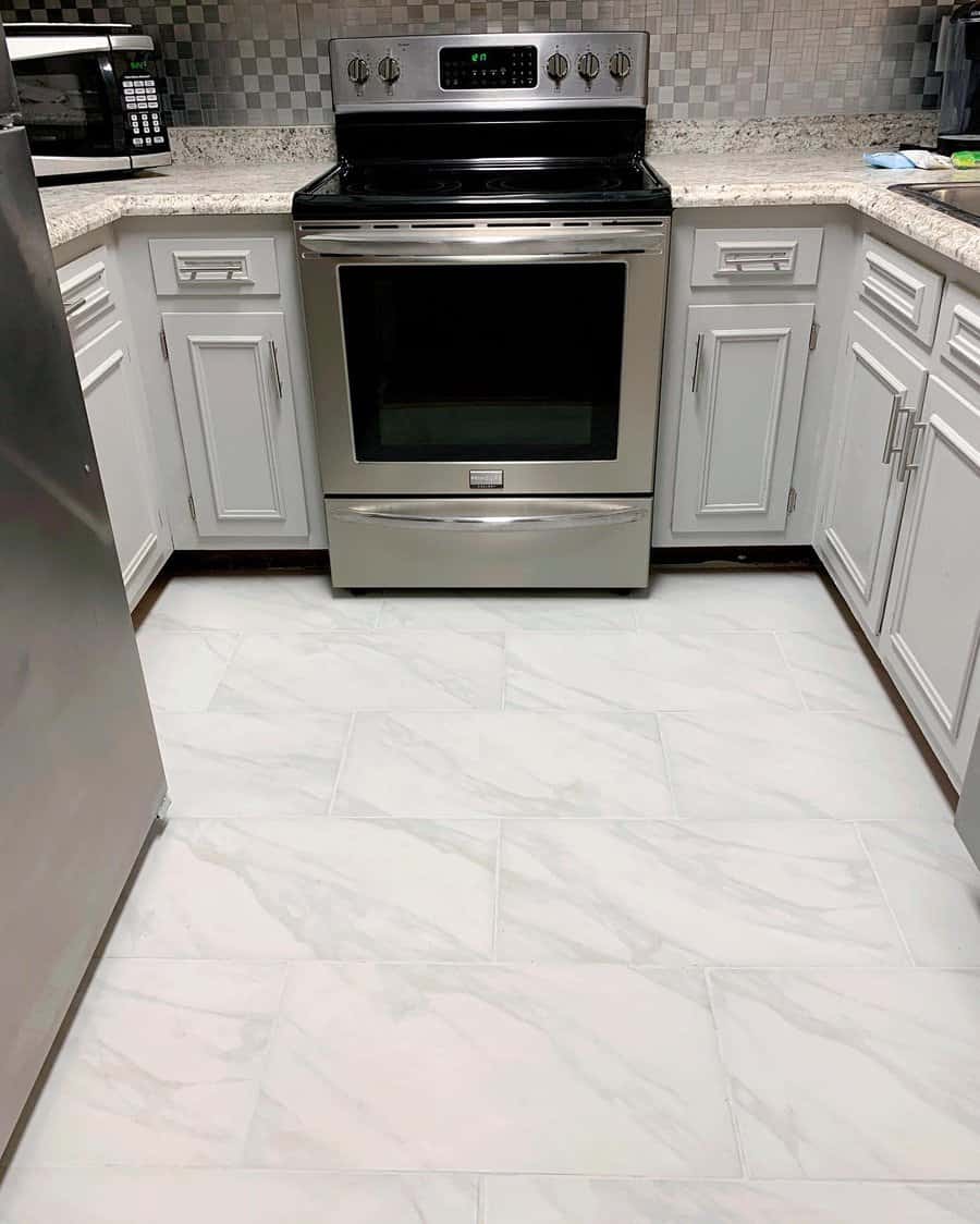 Modern kitchen with stainless steel oven, white cabinets, and light gray marble floor tiles