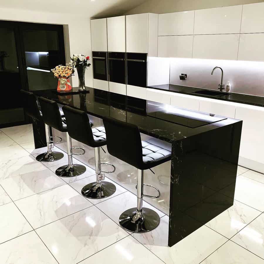 Glossy white marble flooring adds a luxurious touch to this sleek black-and-white kitchen, enhancing its modern and sophisticated aesthetic