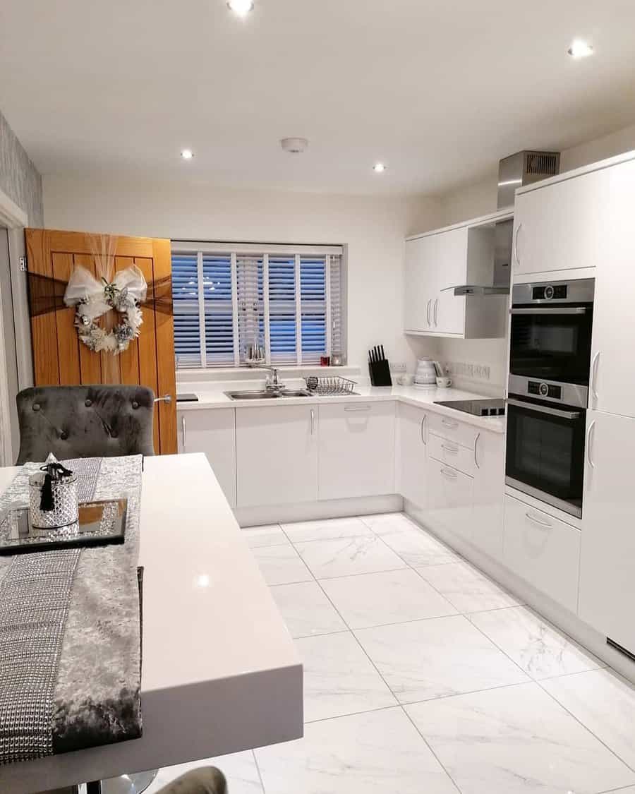 White marble flooring enhances this all-white kitchen, adding elegance and a seamless, luxurious feel with soft veining for subtle texture