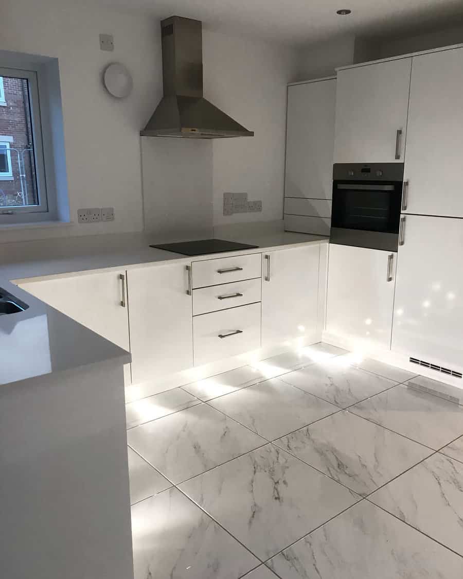 Polished white marble flooring with subtle veining enhances this sleek all-white kitchen, reflecting light for a bright and spacious feel