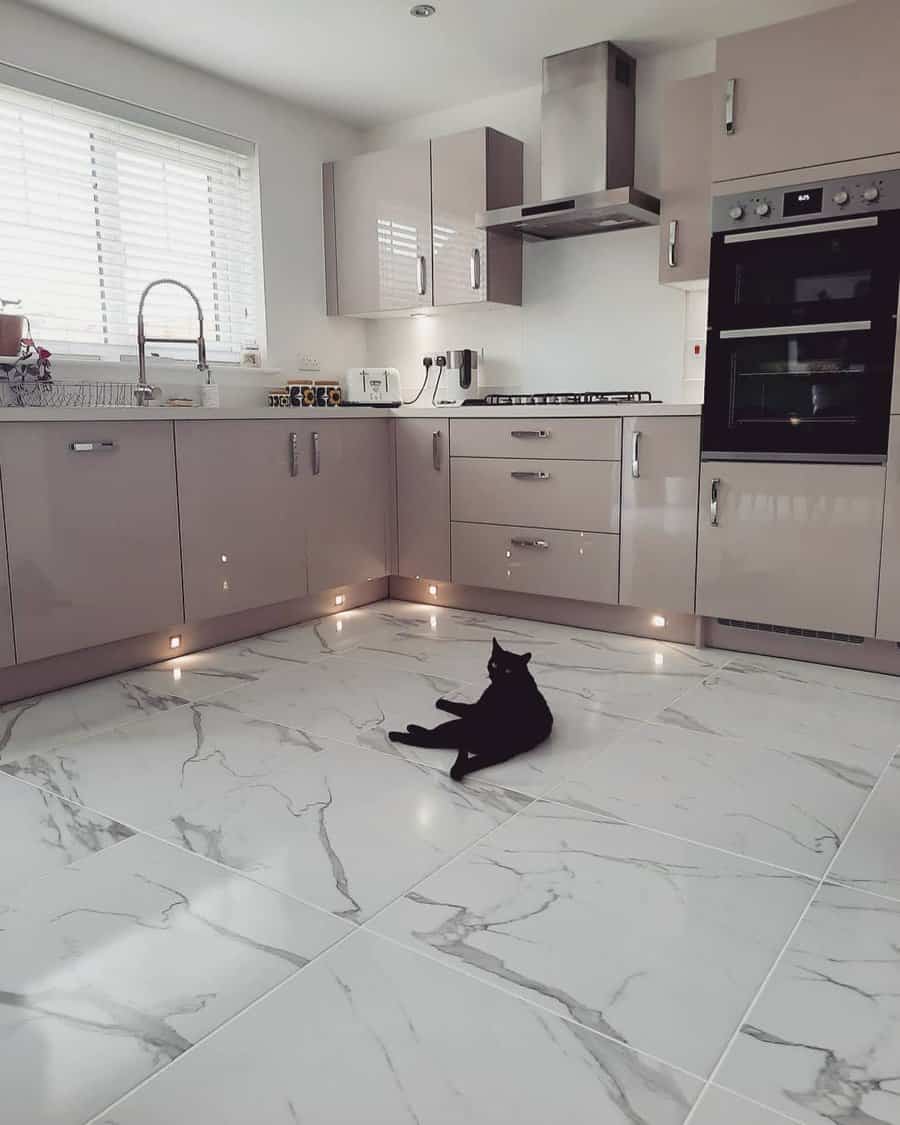 Glossy white marble flooring with grey veining adds elegance to this modern kitchen, complemented by soft-toned cabinetry and ambient lighting