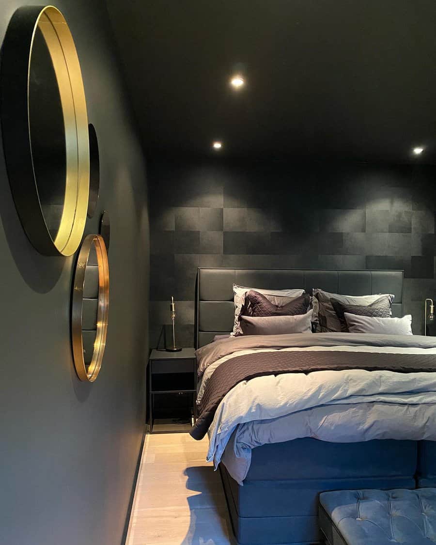 Modern bedroom with dark walls, large bed with layered bedding, and gold circular mirrors on the wall. Soft, recessed lighting above