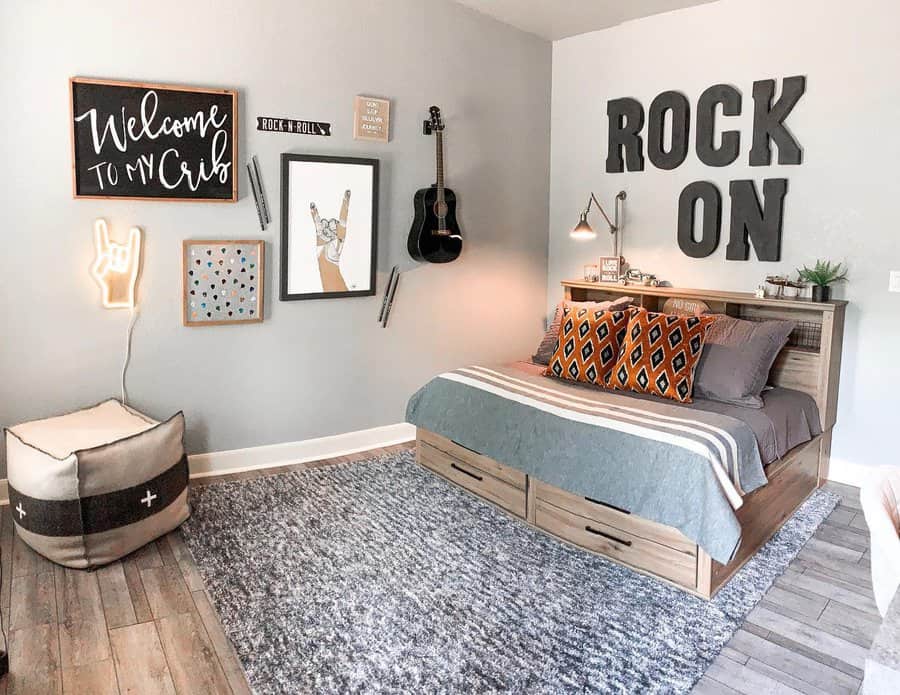 Bedroom with a rock music theme, featuring "Rock On" wall letters, bed with orange pillows, guitar decor, and a neon hand sign