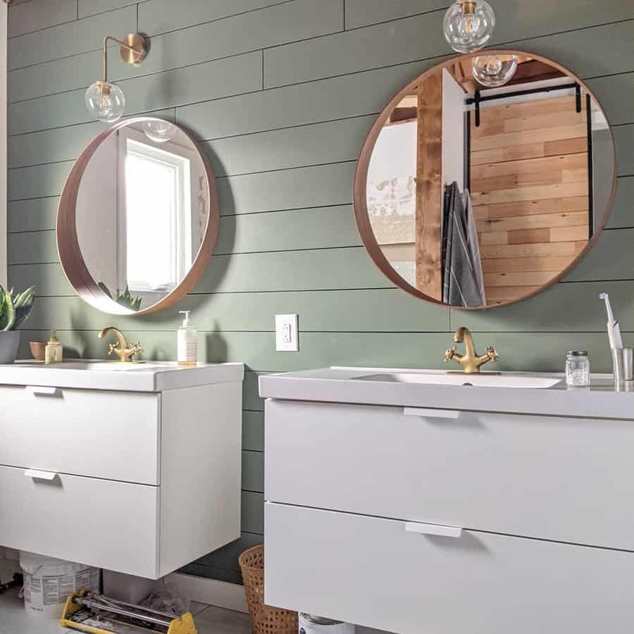 Modern bathroom with green shiplap walls and round mirrors