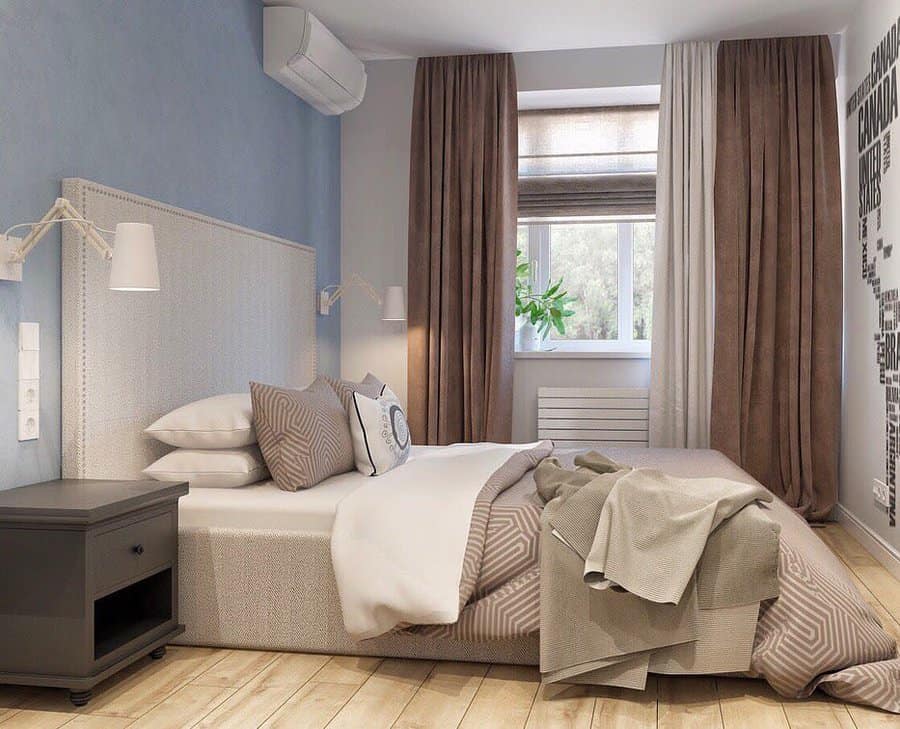 Cozy bedroom with a neatly made bed, light blue wall, gray nightstand, draped beige curtains, and a window with a potted plant