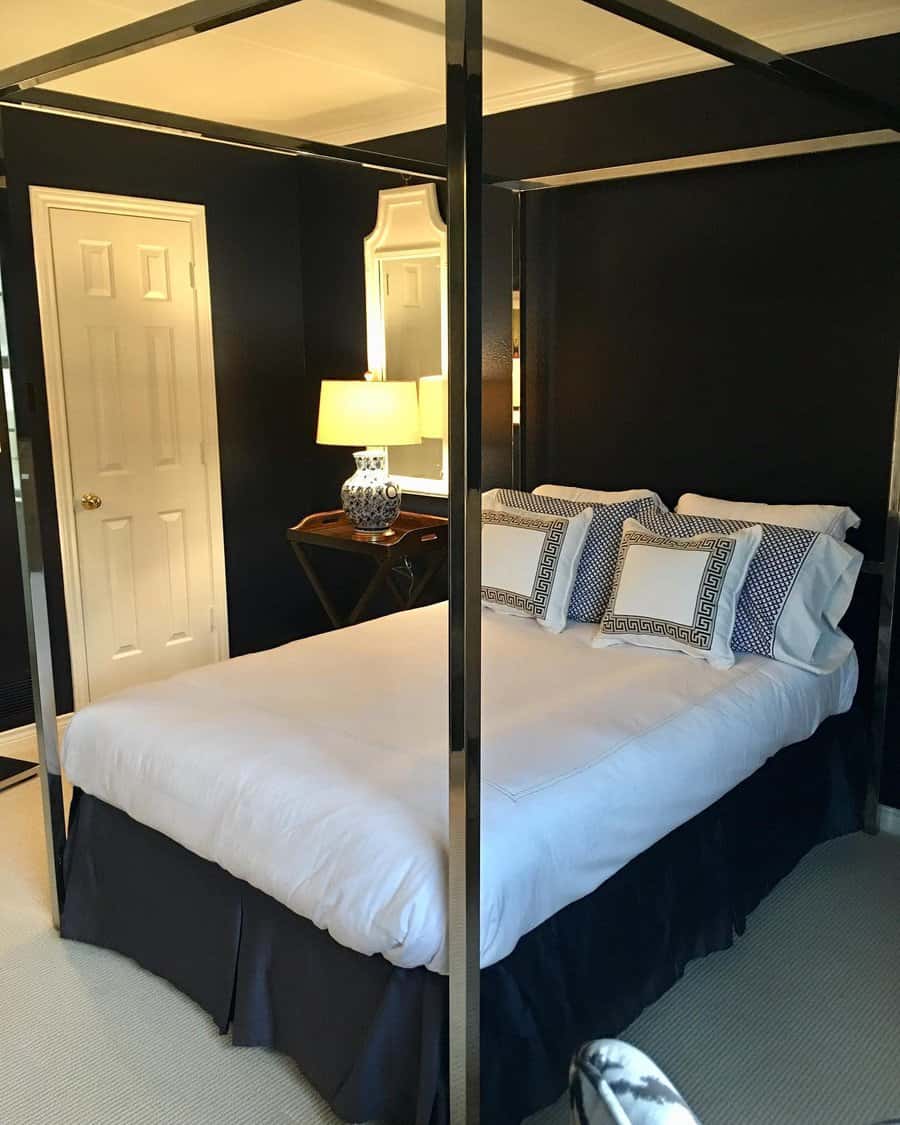 Sophisticated black canopy bed with a sleek metal frame, white bedding, Greek key pillows, and dark walls for a bold and elegant bedroom design