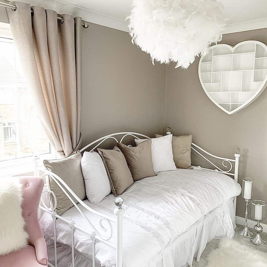 Elegant white metal daybed with plush neutral pillows, a feathered chandelier, and soft decor, creating a dreamy and sophisticated bedroom nook