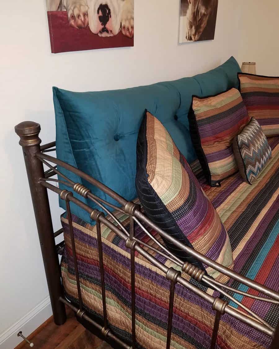 Metal daybed with blue and striped pillows, colorful covers, and pet photos on the wall