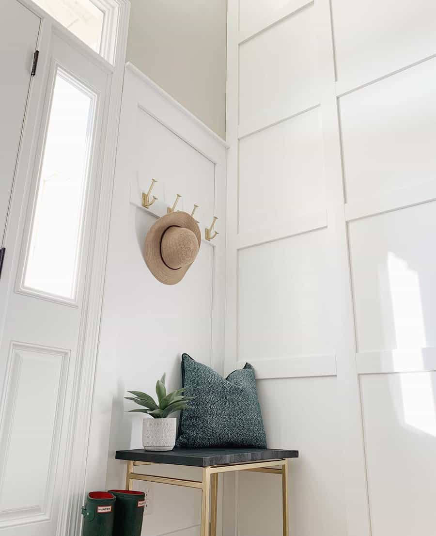 Minimalist entryway with a sleek metal bench, deep green accents, gold hooks, and bright white paneling, creating a modern and elegant space